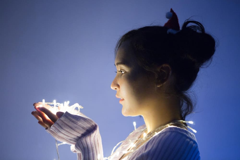Side view of an introverted, beautiful young woman with lights in her hands