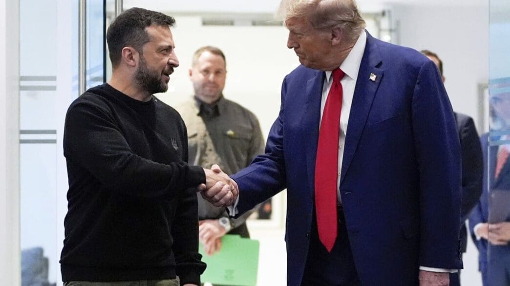 Volodymyr Zelenskyy and President Donald Trump shake hands in an indoor setting, with a serious and focused expression.