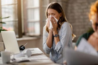 Young sick businesswoman sneezing in a tissue while working in the office