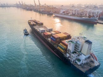 A container ship is arriving at the port, guided by tugboats for a safe entry into the international logistics gateway. By Shutterstock - Iam_Anuphone