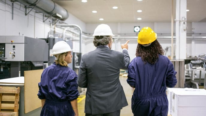 A male engineer and female factory employees in hard hats walking through a US factory floor