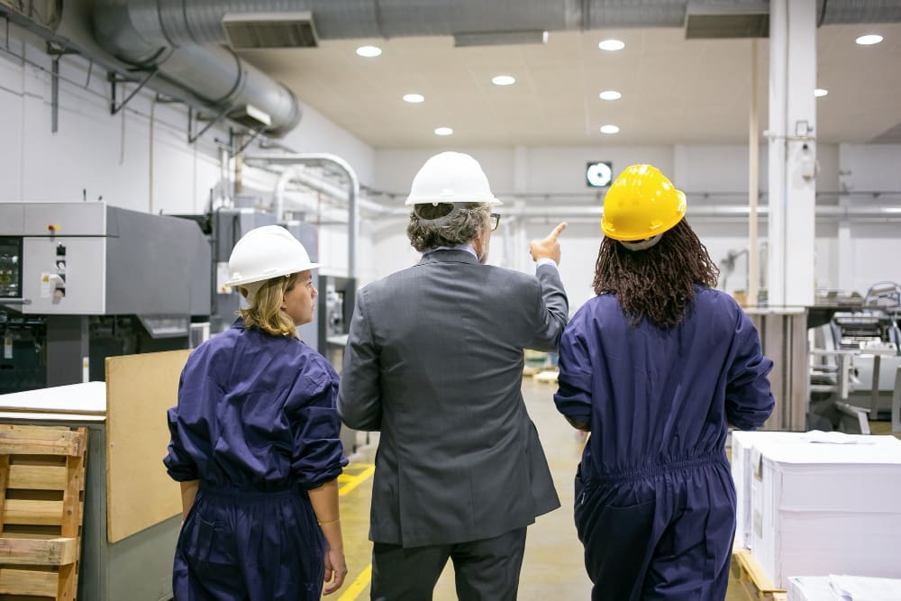 A male engineer and female factory employees in hard hats walking through a US factory floor