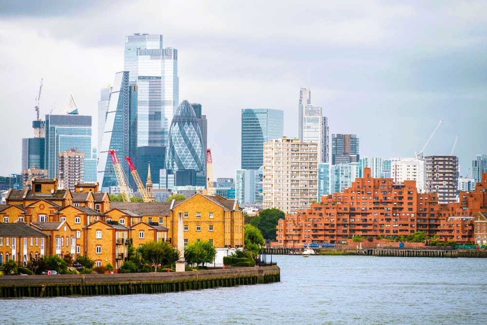 Cityscape of London, UK, featuring the Thames River with a backdrop of financial and residential buildings