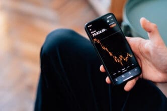 Close-up shot of a male hand holding a smartphone displaying declining cryptocurrencies