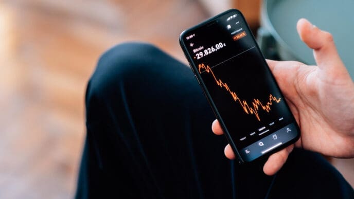 Close-up shot of a male hand holding a smartphone displaying declining cryptocurrencies