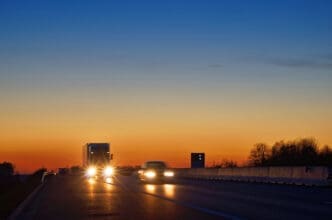 Highway with oncoming trucks and a car after sunset. Shining the spotlight cars. By Shutterstock - Milos Muller