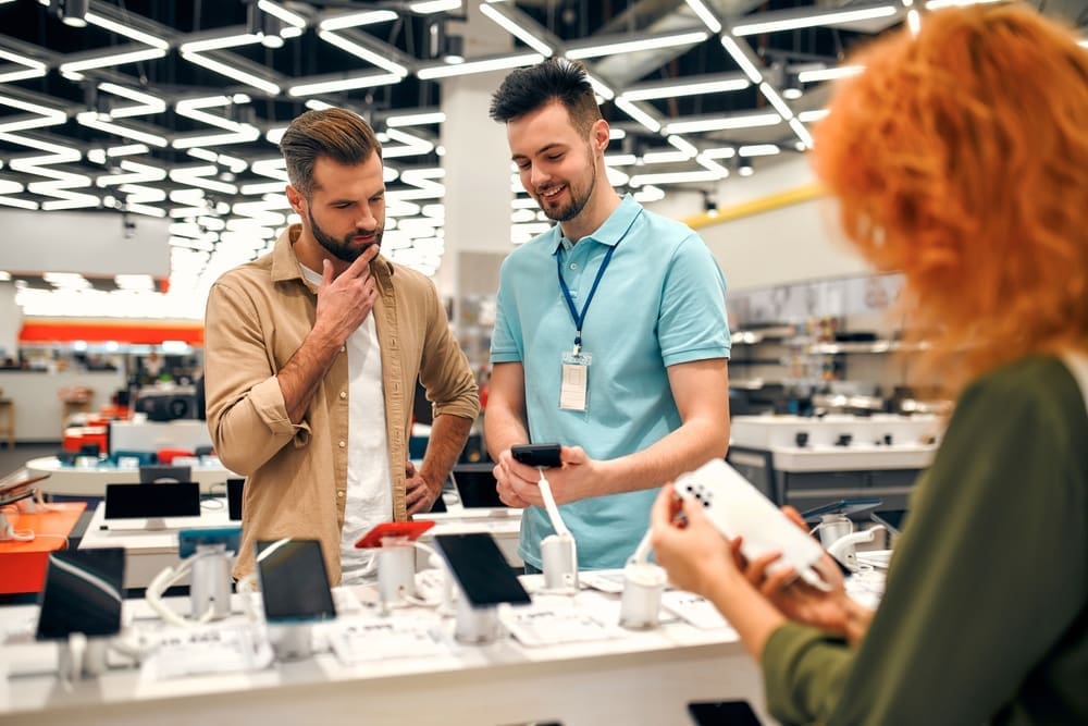 Sales consultant advises man who chooses new smartphone in store of household appliances, electronics and gadgets. By Shutterstock - ORION PRODUCTION