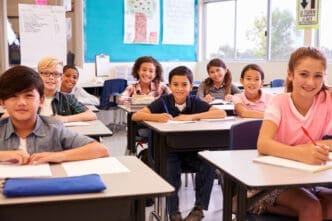 Smiling elementary school kids sitting at desks in classroom. By Shutterstock.com - Monkey Business Images