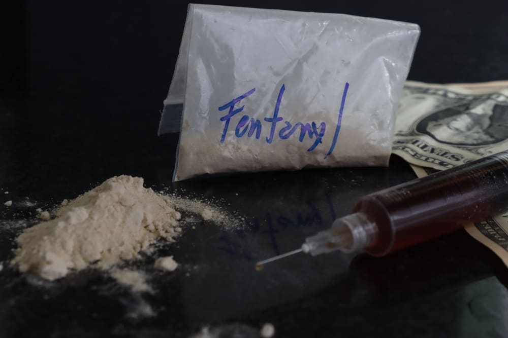 Dollar bills and a fentanyl powder pack with a syringe in a dark place showing the addiction of drugs