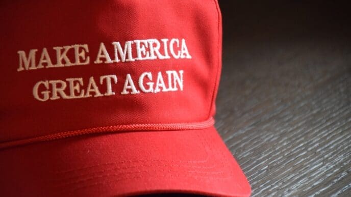 Indianapolis, IN - March 2, 2020. A Donald J. Trump Make America Great Again hat staged on a wooden table from the 2020 Presidential campaign. By Shutterstock - Shelby Griffith