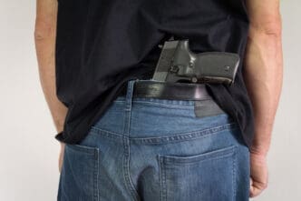 Man hiding the gun behind his back. Illegal possession of weapons. By Shutterstock.com - Zoka74