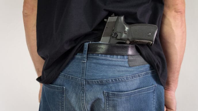 Man hiding the gun behind his back. Illegal possession of weapons. By Shutterstock.com - Zoka74