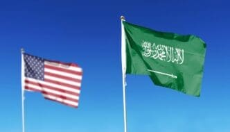 Saudi Arabia flag flutters in the clear sky. Flying in the sky. The American flag in the distance is intentionally blurred in the photo. By Shutterstock.com - Andy.LIU