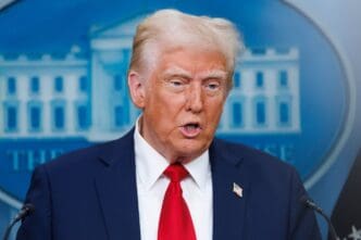 A close-up portrait of Donald Trump speaking at a podium, wearing a dark suit and red tie, with a blurred blue backdrop featuring a stylized White House building.