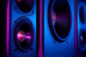 Two sound speakers and subwoofer on dark background with neon lights. Set for listening music. Audio equipment