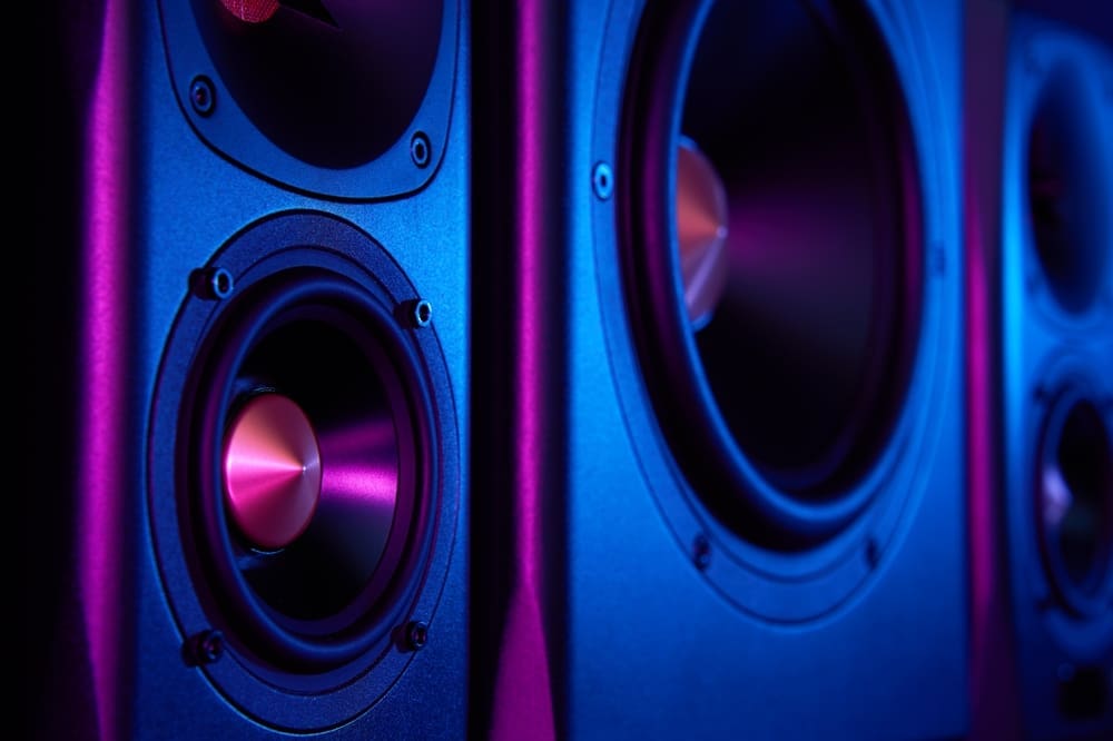 Two sound speakers and subwoofer on dark background with neon lights. Set for listening music. Audio equipment