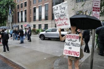 A protester holds two signs, one saying "First They Came For KILMAR," and another saying "DETENTION without DUE PROCESS IS KIDNAPPING" while standing in the rain.