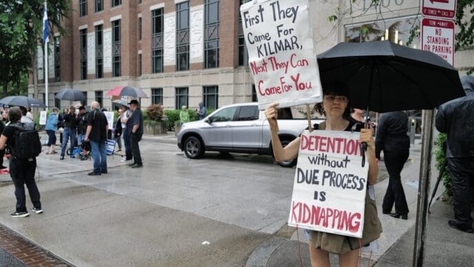 A protester holds two signs, one saying "First They Came For KILMAR," and another saying "DETENTION without DUE PROCESS IS KIDNAPPING" while standing in the rain.