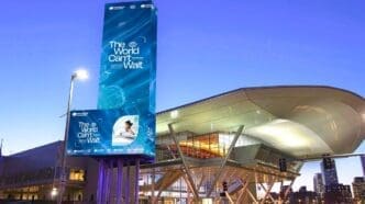 The exterior of the Boston Convention and Exhibition Center at dusk, with its large digital marquee lit up for the BIO International Convention, displaying the slogan "The World Can't Wait."