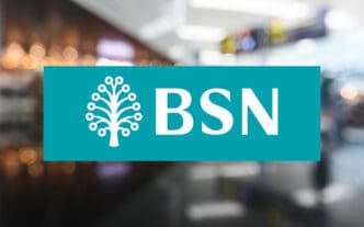 The BSN (Bank Simpanan Nasional) logo, featuring a stylized white tree icon and the letters "BSN" on a teal rectangle, superimposed over a blurry photo of a modern building interior.
