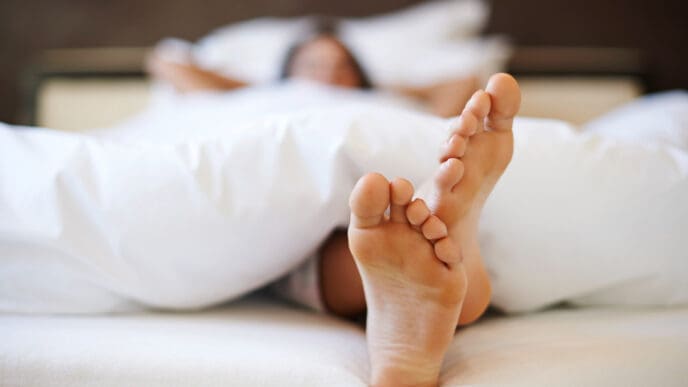 A beautiful woman is in bed, doing 'cricket feet' as she falls asleep.