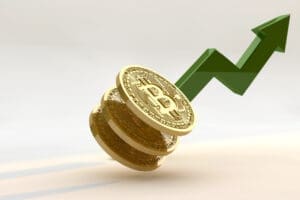 A 3D rendering of three golden Bitcoin coins stacked on a light surface, with a large green arrow rising sharply upwards behind them, symbolizing cryptocurrency growth.