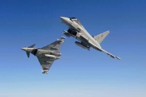 Two Royal Air Force (RAF) Eurofighter Typhoon fighter jets flying in close formation against a clear, solid blue sky. One jet is banked, showing its top side, while the other is seen from below.