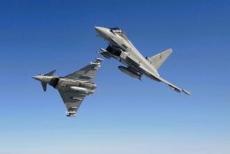 Two Royal Air Force (RAF) Eurofighter Typhoon fighter jets flying in close formation against a clear, solid blue sky. One jet is banked, showing its top side, while the other is seen from below.