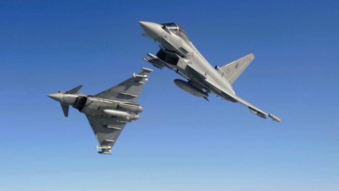 Two Royal Air Force (RAF) Eurofighter Typhoon fighter jets flying in close formation against a clear, solid blue sky. One jet is banked, showing its top side, while the other is seen from below.