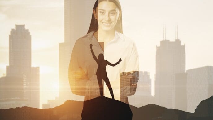 A double exposure image featuring a smiling professional woman with her arms crossed, blended with a city skyline at sunset. A second silhouette of a person in a victory pose on a mountaintop is visible within her figure.