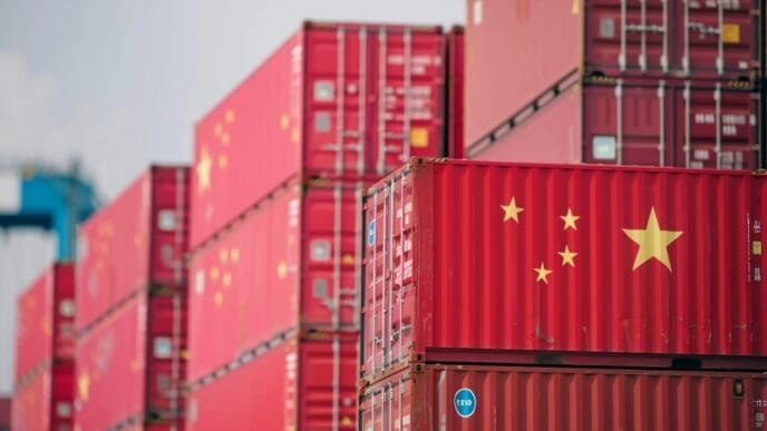 A close-up photo of a red shipping container marked with the flag of China, stacked among many other containers at a busy shipping port.