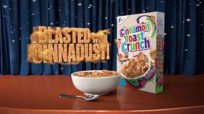 A commercial product shot of Cinnamon Toast Crunch cereal, featuring a full bowl of cereal and the product box on a stage. A large 3D text graphic reads, "BLASTED with CINNADUST!" against a sparkly blue curtain background.