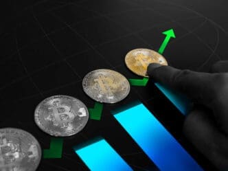 A conceptual image showing physical Bitcoin coins placed on a rising blue bar chart. A person's finger pushes a golden Bitcoin upwards along a green arrow, symbolizing investment and growth.