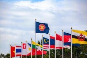 The national flags of the ten member countries of the Association of Southeast Asian Nations (ASEAN), alongside the official ASEAN flag, waving together on flagpoles against a clear blue sky.