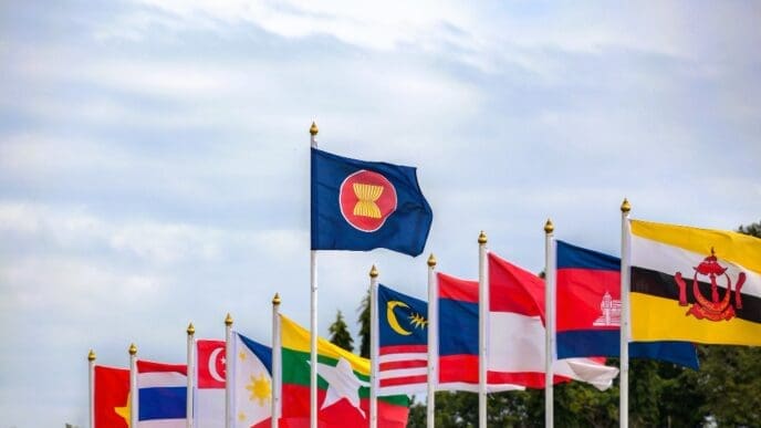 The national flags of the ten member countries of the Association of Southeast Asian Nations (ASEAN), alongside the official ASEAN flag, waving together on flagpoles against a clear blue sky.