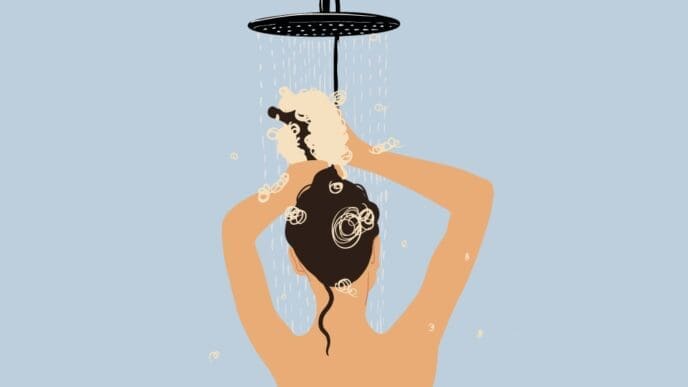 A stylized illustration of a person with dark hair seen from behind, washing their hair with shampoo lather under a shower head against a light blue background.