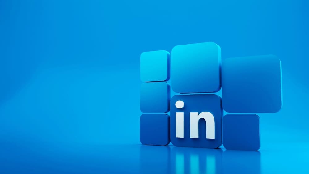 A 3D rendering of the LinkedIn logo, composed of blue squares with the white letters "in" on the front, set against a solid blue background with a reflective surface.