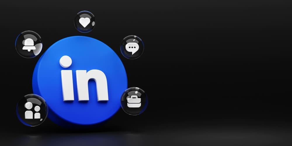 A 3D rendering of the circular LinkedIn logo surrounded by floating glass spheres containing other icons like a heart, a notification bell, a briefcase for jobs, a speech bubble, and a network icon.