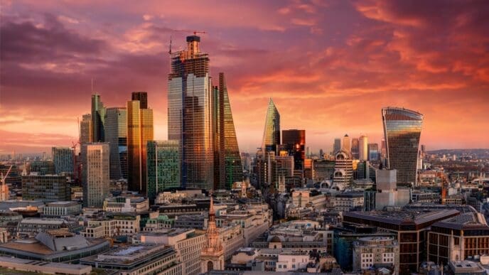 The modern skyscrapers of the London financial district, such as the Gherkin and the Walkie-Talkie building, are silhouetted against a dramatic and colorful sunset sky.
