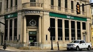 The M&T Bank building in Tamaqua, Pennsylvania, a large, historic stone structure with classical columns, a rounded corner entrance featuring a prominent integrated clock, and green awnings.