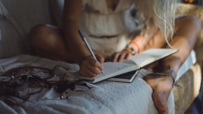A happy young woman sits in a cozy, comfortable room, smiling as she focuses on writing or drawing in a notebook.