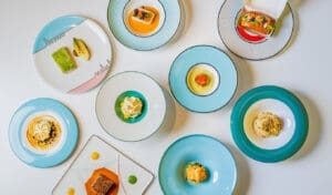 A top-down view of multiple small, artfully plated dishes from Torno Subito Miami. The vibrant food creations are presented on various colorful, uniquely designed plates with distinct patterns.