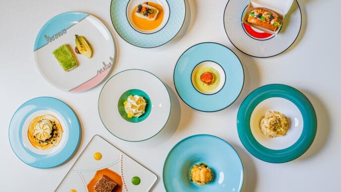 A top-down view of multiple small, artfully plated dishes from Torno Subito Miami. The vibrant food creations are presented on various colorful, uniquely designed plates with distinct patterns.