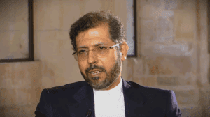 A professional portrait of Saeed Khatibzadeh, an Iranian diplomat with dark hair, a beard, and glasses, wearing a dark suit and white shirt, appearing to be speaking during an interview.