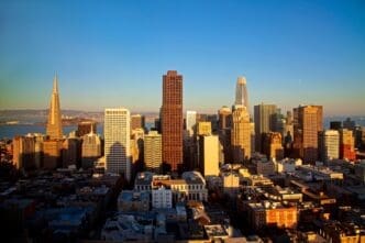 A scenic photograph of the San Francisco skyline at golden hour, featuring the iconic Transamerica Pyramid and other skyscrapers of the Financial District under a clear blue sky.