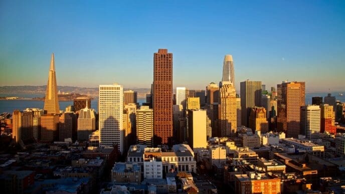 A scenic photograph of the San Francisco skyline at golden hour, featuring the iconic Transamerica Pyramid and other skyscrapers of the Financial District under a clear blue sky.