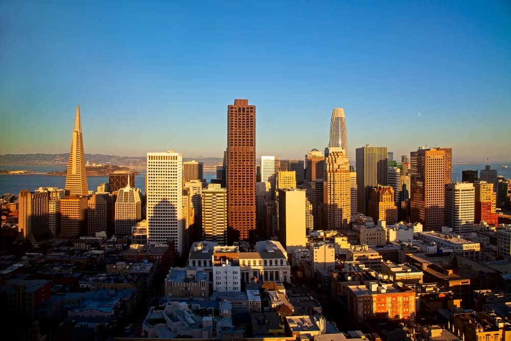 A scenic photograph of the San Francisco skyline at golden hour, featuring the iconic Transamerica Pyramid and other skyscrapers of the Financial District under a clear blue sky.