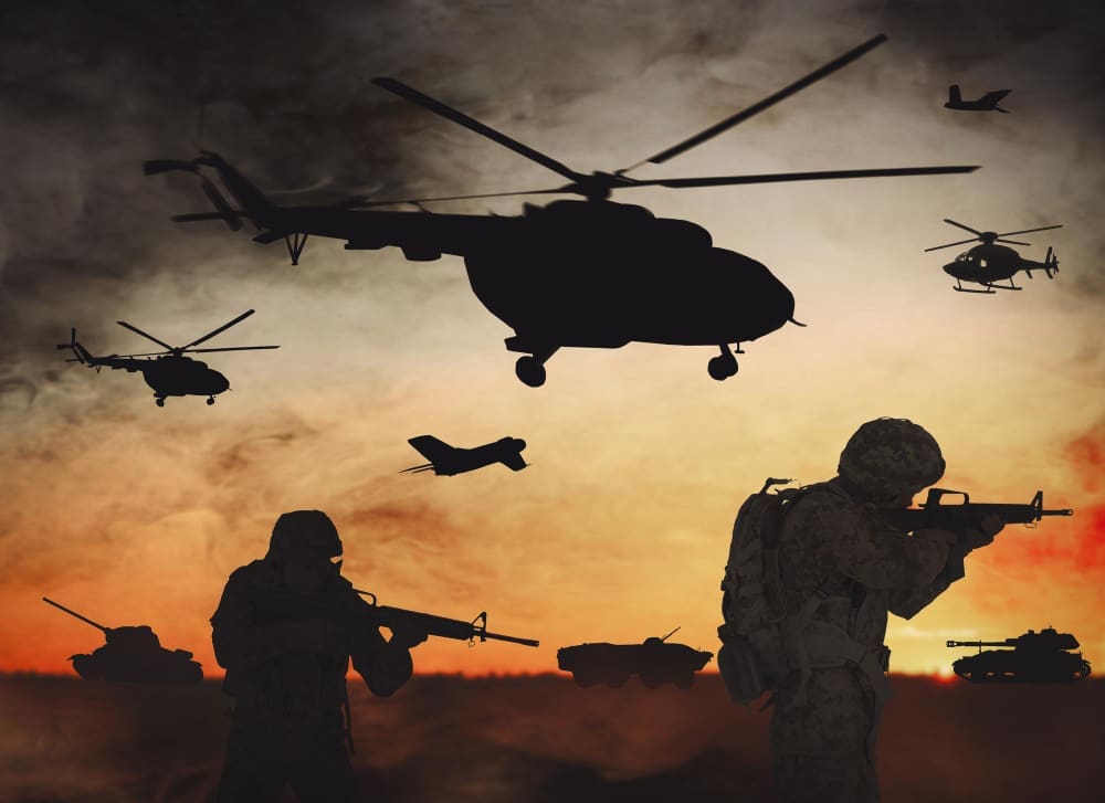 A silhouette of a battle scene against a hazy sunset, featuring soldiers with rifles in the foreground, with tanks on the ground and multiple military helicopters and a jet flying overhead.