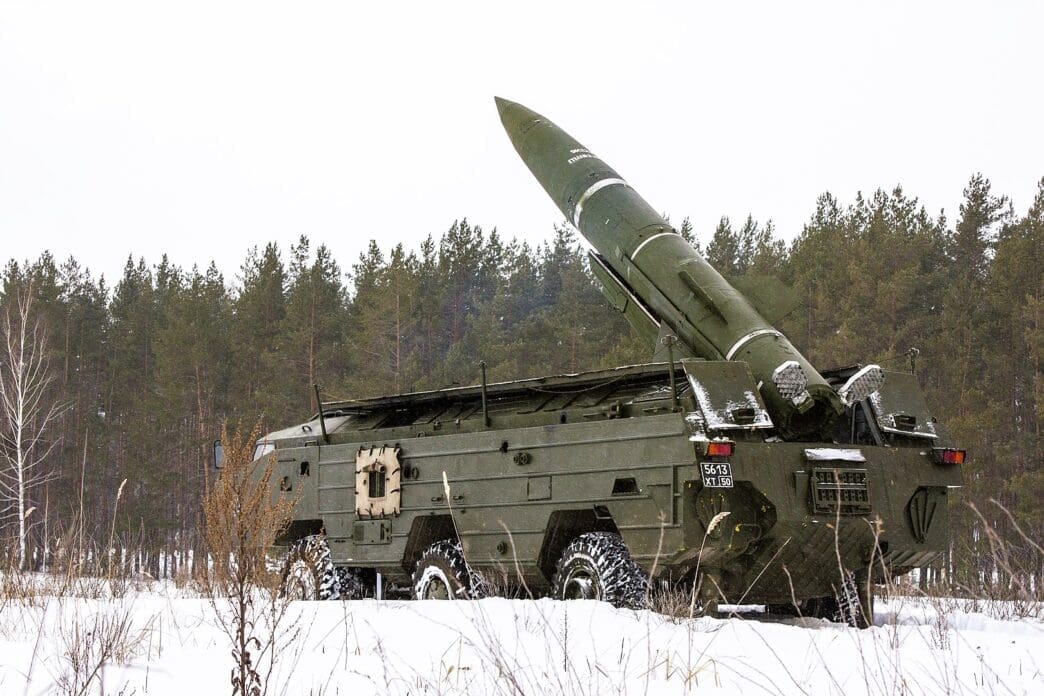 A Soviet OTR-21 Tochka tactical ballistic missile is mounted on its large, multi-wheeled military launcher vehicle, angled upwards in a snowy, forested landscape.