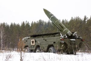 A Soviet OTR-21 Tochka tactical ballistic missile is mounted on its large, multi-wheeled military launcher vehicle, angled upwards in a snowy, forested landscape.